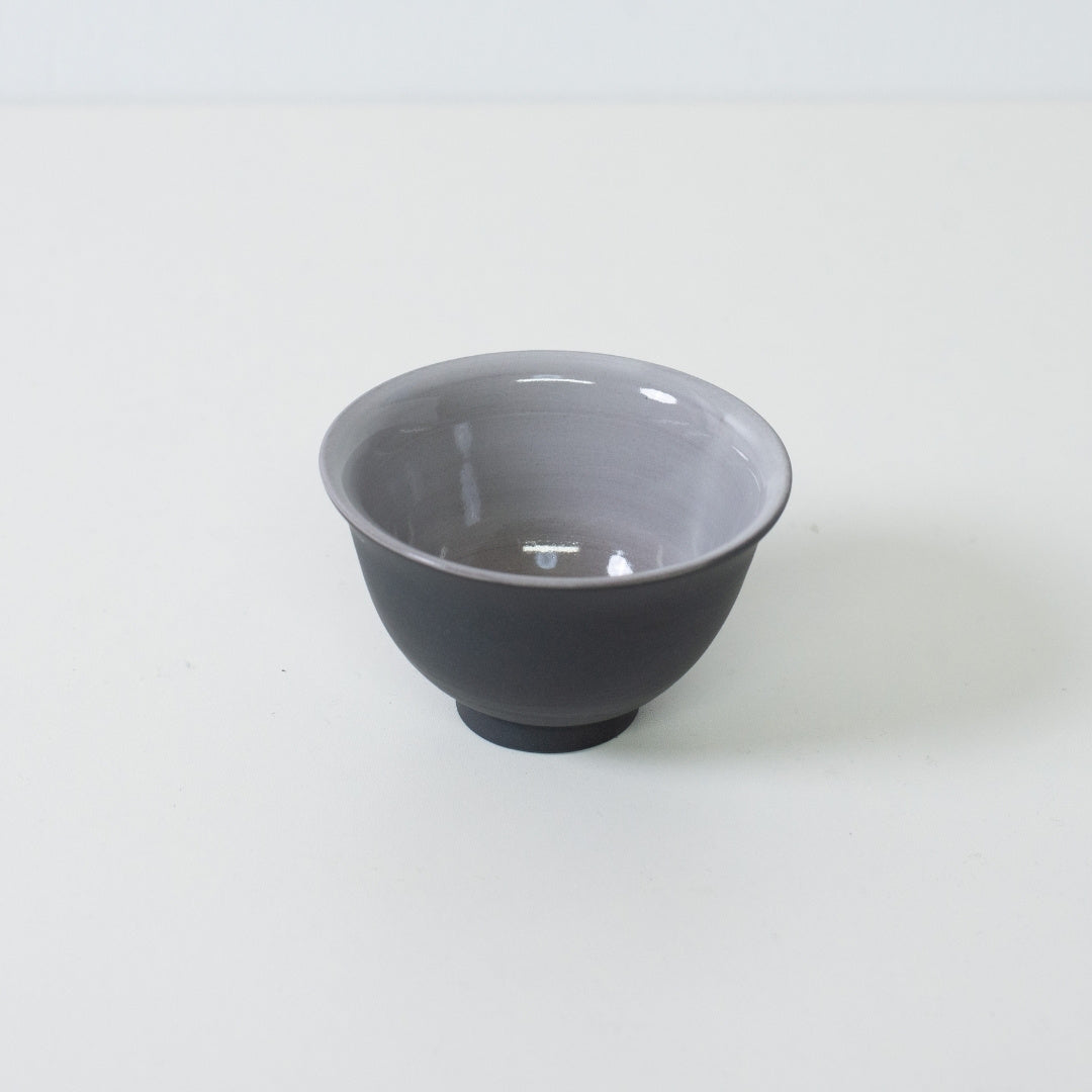 Angled view of black japanese tea cup revealing grey glazed interior designed to highlight tea color.