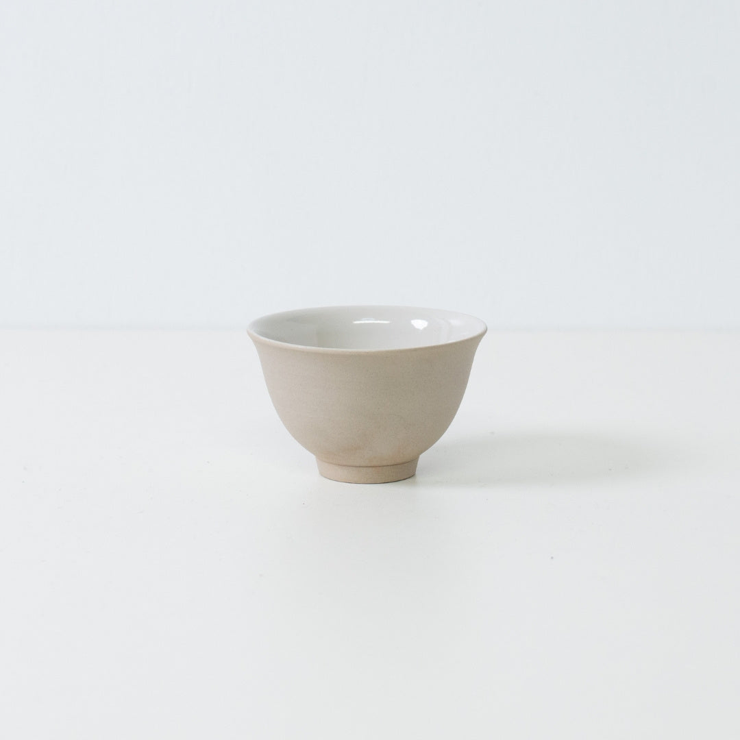 Profile view of a single beige kumidashi Japanese tea cup with a matte stoneware texture