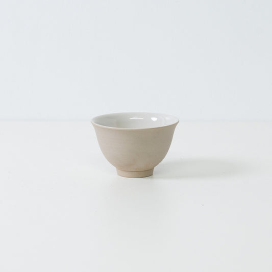 Profile view of a single beige kumidashi Japanese tea cup with a matte stoneware texture