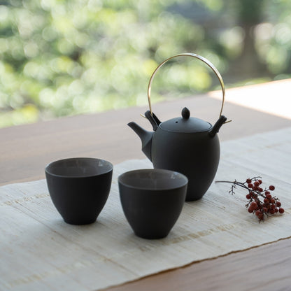 Black Japanese tea set with kyusu on a wooden table for tea lovers enjoying a modern zen ritual.