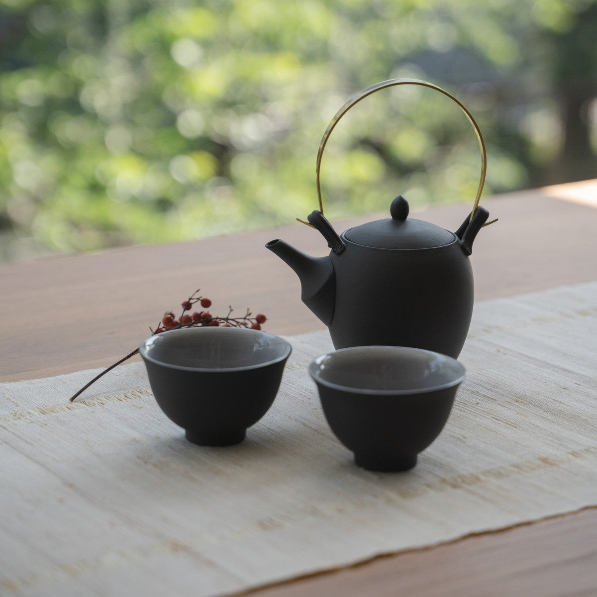 Black Japanese teapot "Donguri" and Japanese tea cups on a linen runner for wellness seekers relaxing with tea.