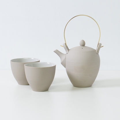 Modern japanese tea set displaying a white clay kyusu teapot with brass handle alongside two curved f shape tea cups