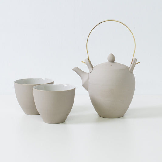 Modern japanese tea set displaying a white clay kyusu teapot with brass handle alongside two curved f shape tea cups