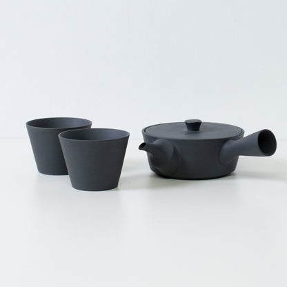 Modern black japanese tea set with a flat sencha kyusu teapot and cone shaped tea cups on a white table