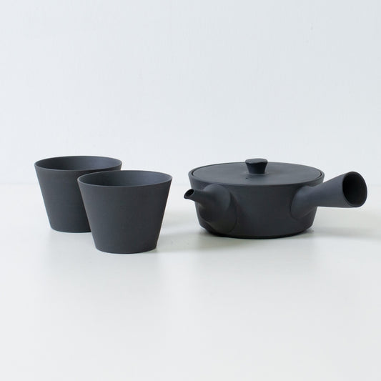 Modern black japanese tea set with a flat sencha kyusu teapot and cone shaped tea cups on a white table