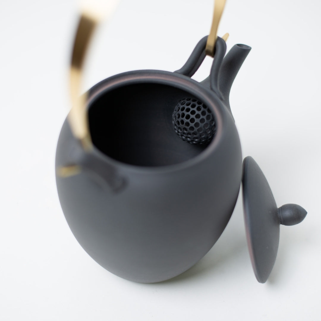 Inside view of a donguri japanese teapot displaying the ball shaped ceramic strainer and brass handle attachment
