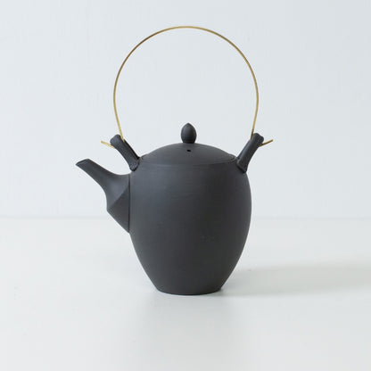 Side view of a black japanese teapot with an acorn shape and brass handle showcasing traditional banko ware craftsmanship