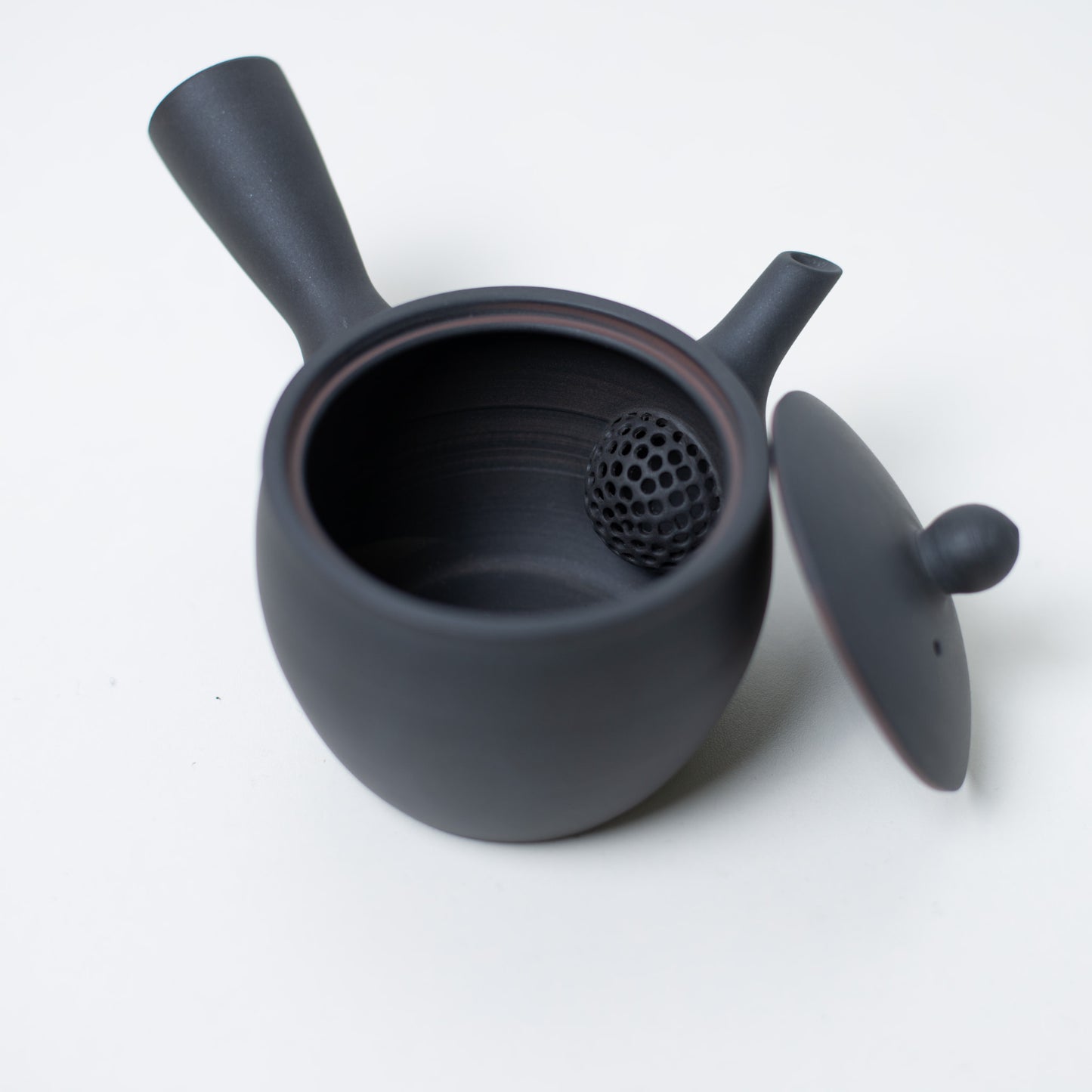 Open japanese teapot looking inside at the ceramic mesh strainer and lid of the black kyusu teapot