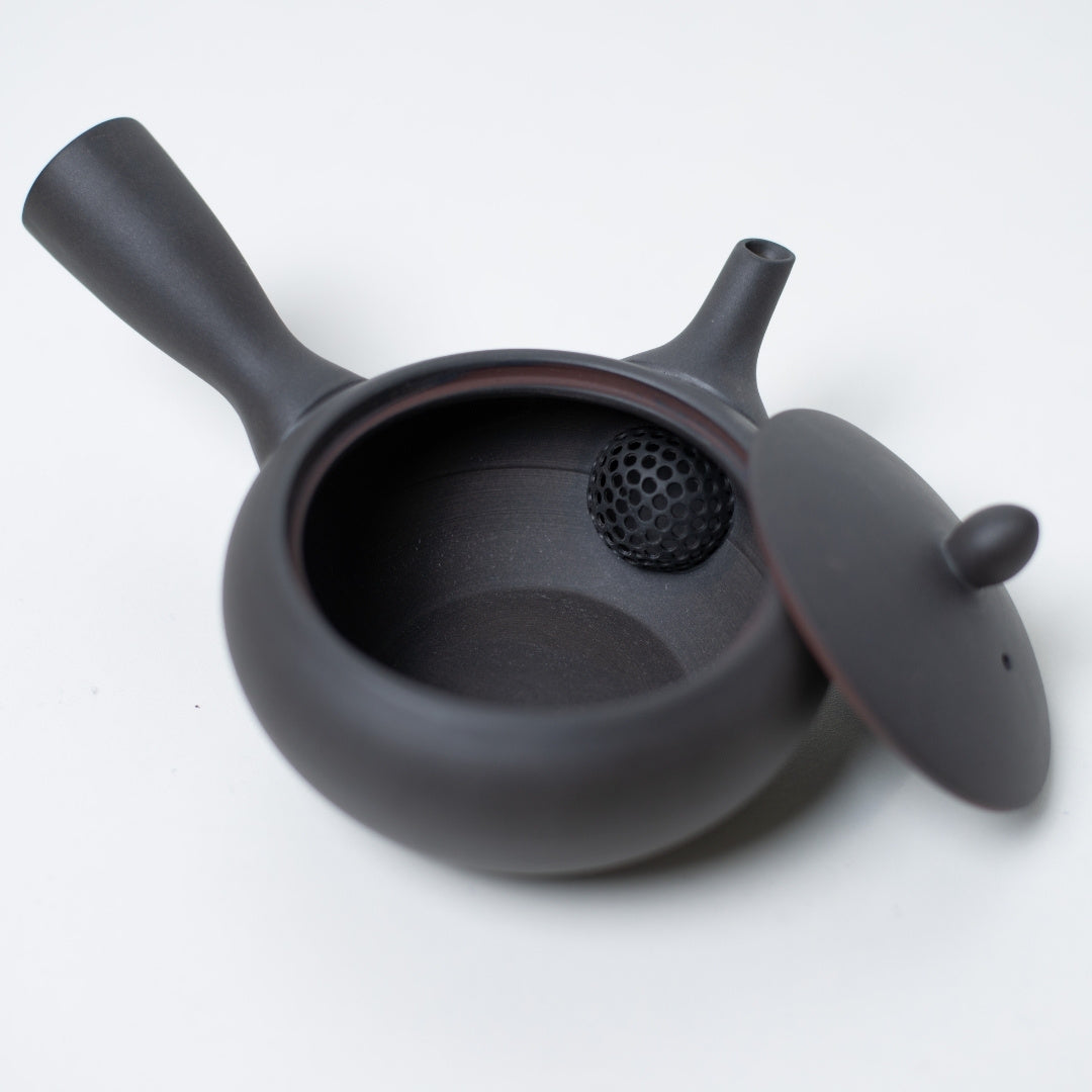 Open black japanese teapot displaying the unglazed interior and ceramic mesh strainer with the lid resting aside.