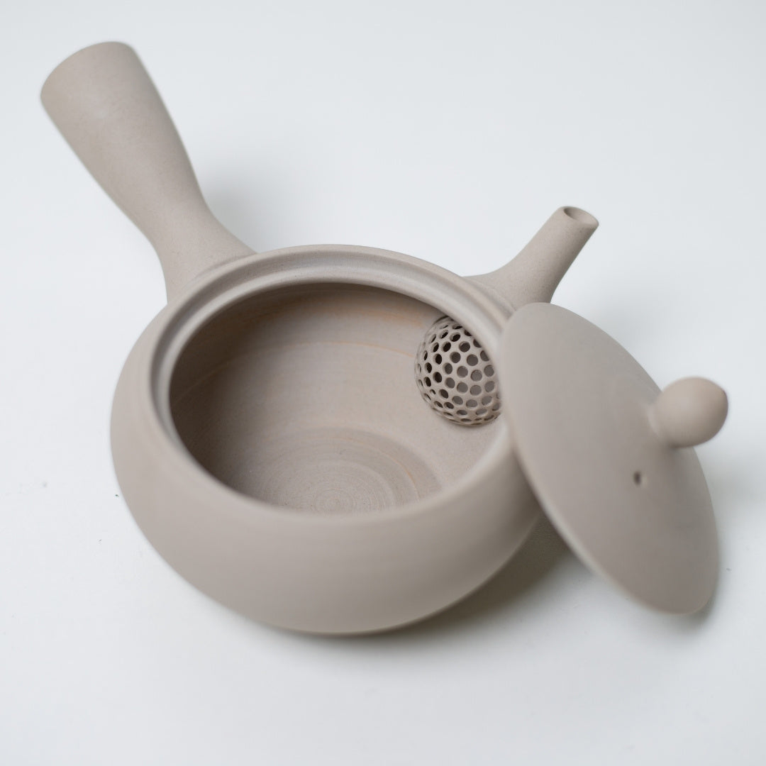 High angle view of an open white japanese teapot revealing the built in strainer mesh and unglazed interior.
