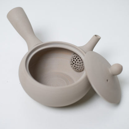 High angle view of an open white japanese teapot revealing the built in strainer mesh and unglazed interior.