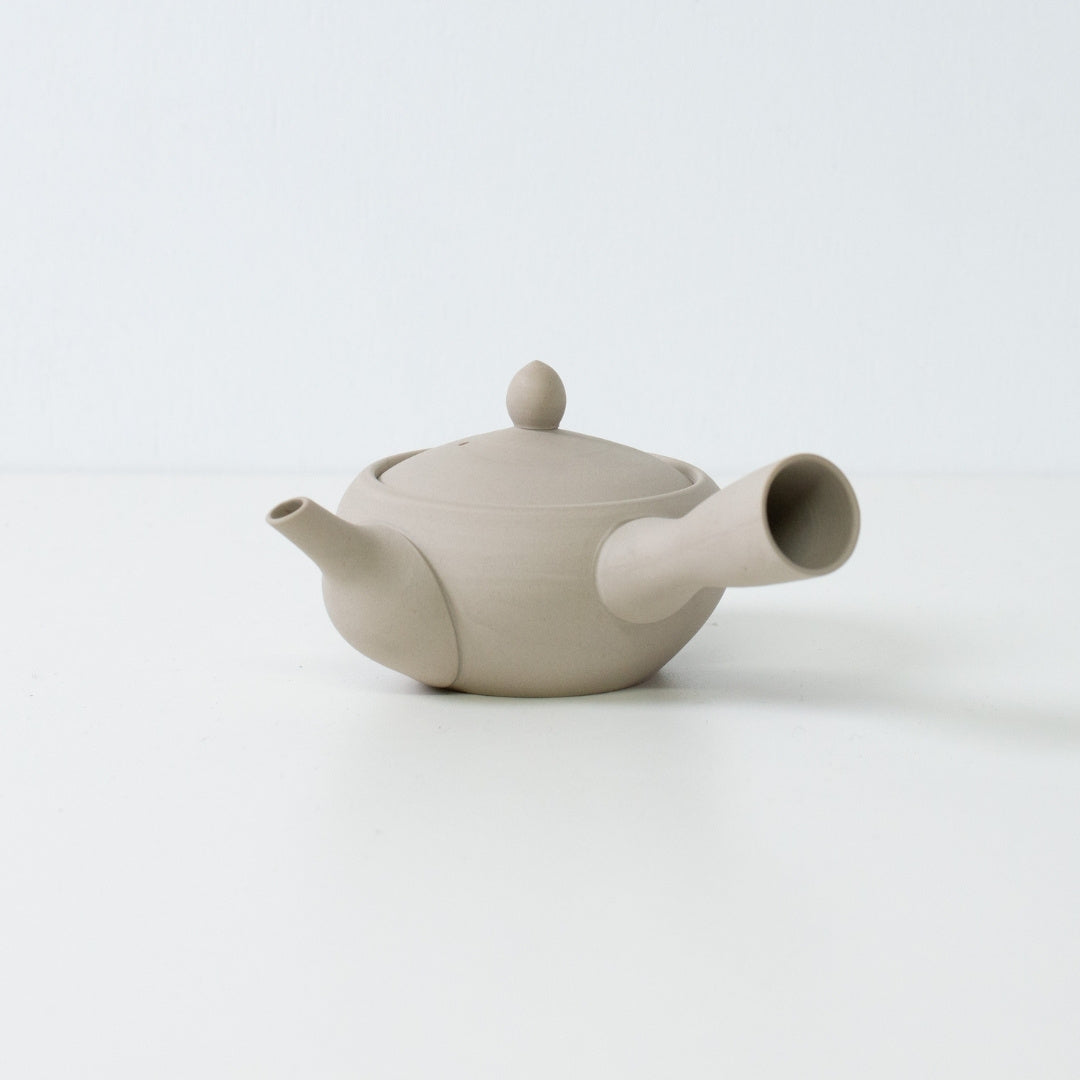 Théière japonaise blanche minimaliste en forme de bol de moine en argile non émaillée sur une surface blanche épurée.