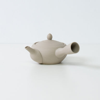 Minimalist white japanese teapot in monks bowl shape made of unglazed clay on a clean white surface.