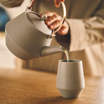 Hand pouring Japanese green tea from a modern Japanese teapot into a yunomi tea cup
