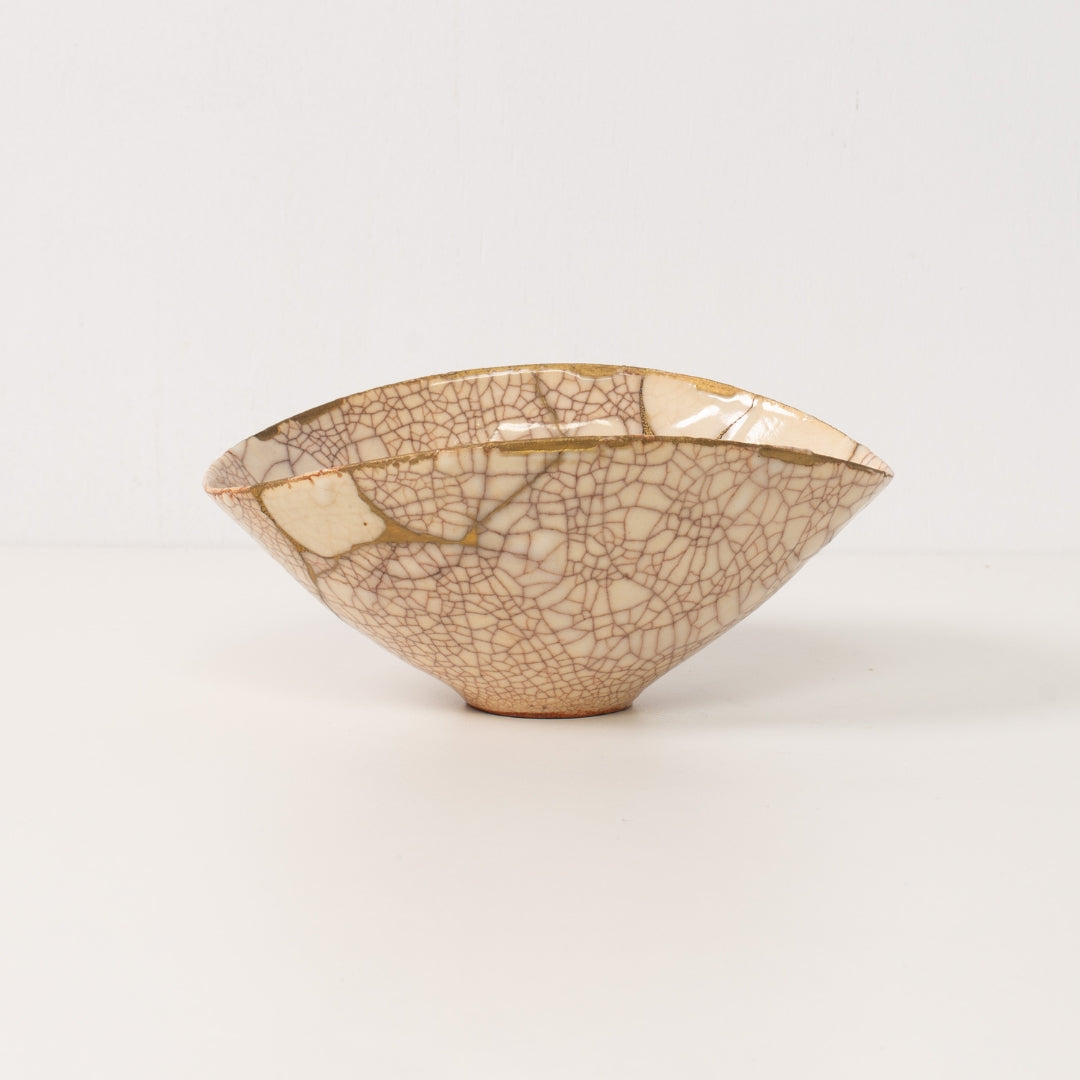 A handcrafted white kintsugi bowl stands on a table displaying gold lines of authentic pottery art