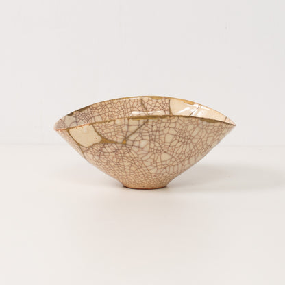 A handcrafted white kintsugi bowl stands on a table displaying gold lines of authentic pottery art