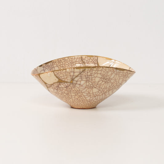 A handcrafted white kintsugi bowl stands on a table displaying gold lines of authentic pottery art