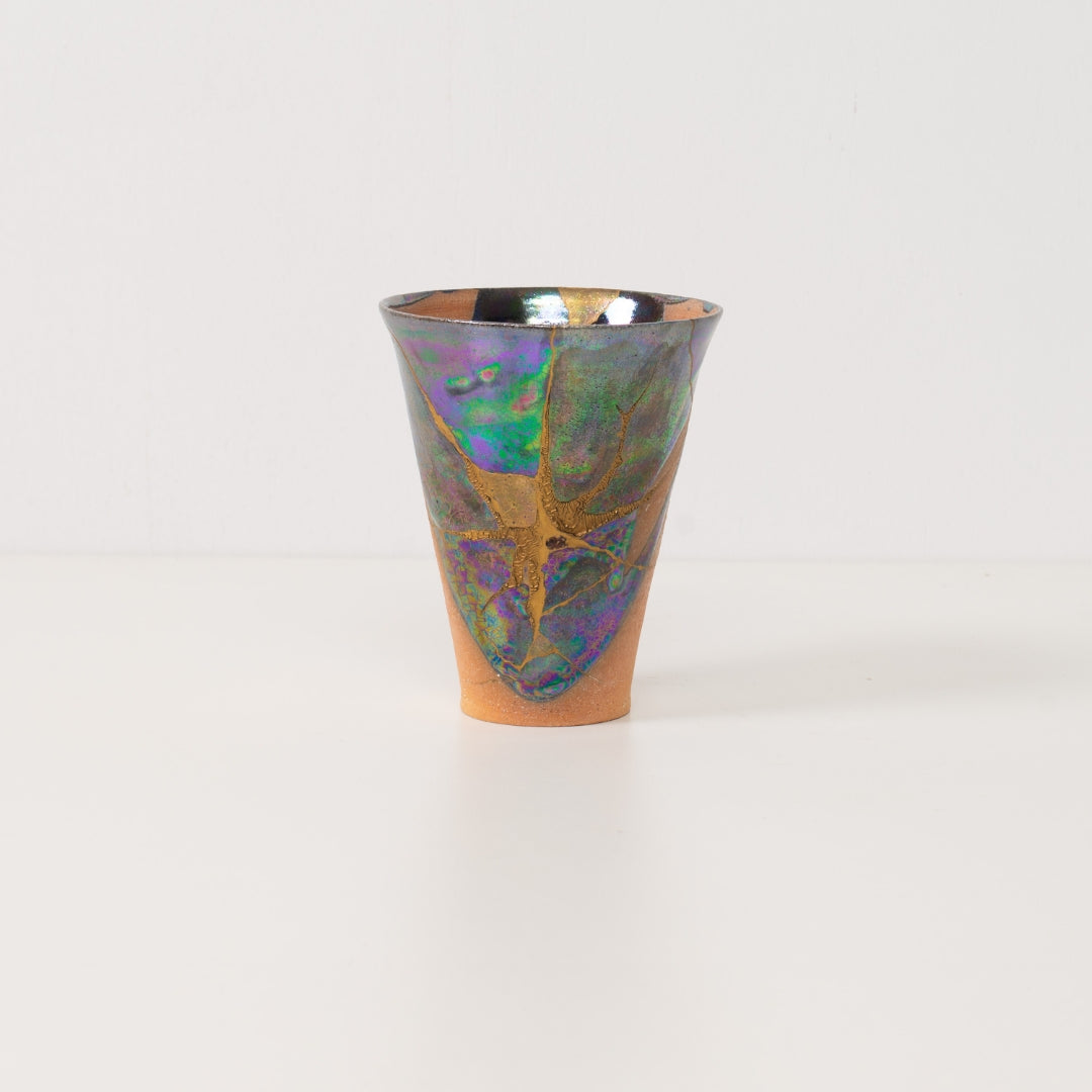 An authentic kintsugi cup stands alone highlighting colorful metallic glazes that define this beautiful kintsugi pottery