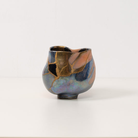 A tall handcrafted kintsugi matcha bowl with colorful glazes and golden mends stands alone on a white table