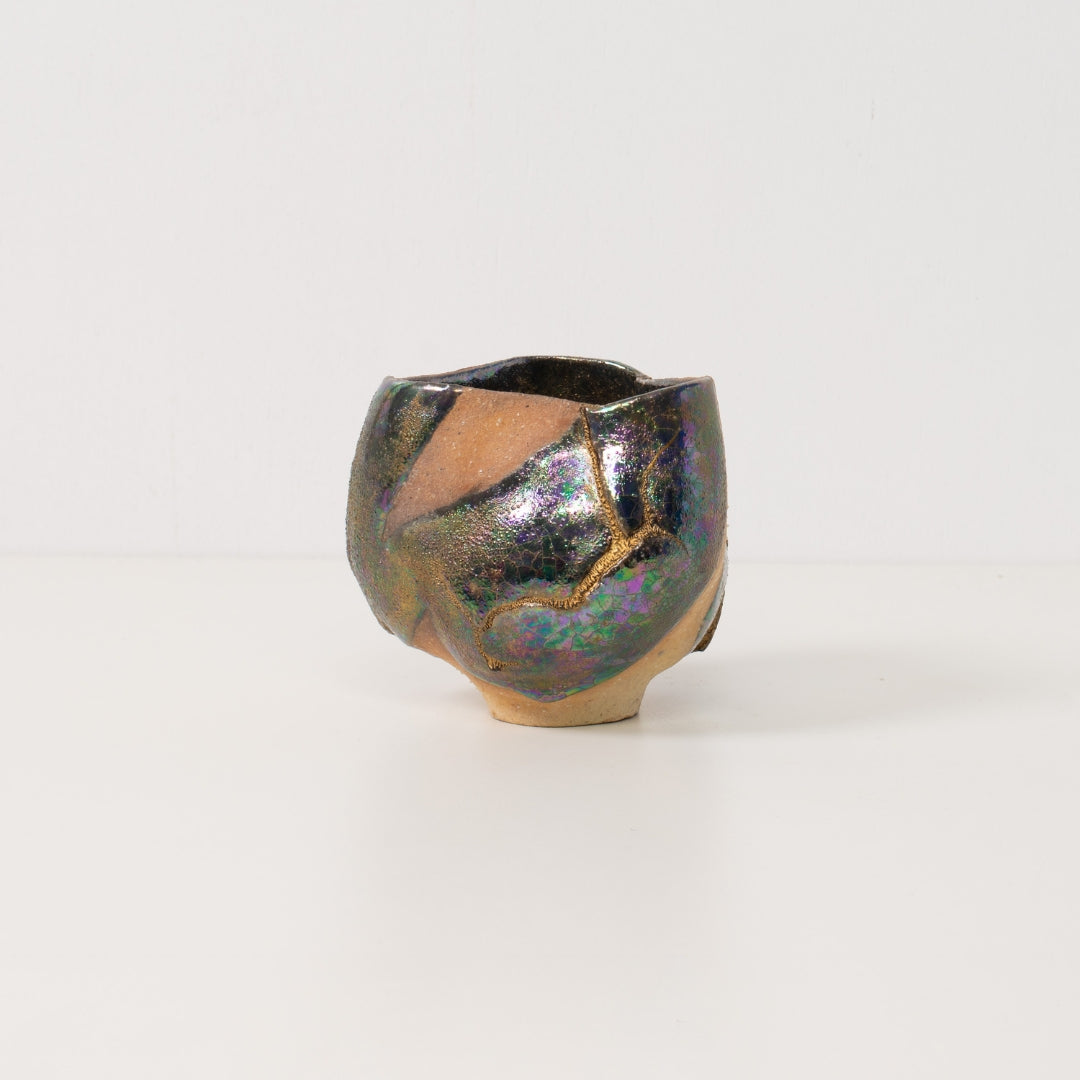 A wide iridescent kintsugi matcha bowl stands alone highlighting vibrant metallic tones that define kintsugi pottery art