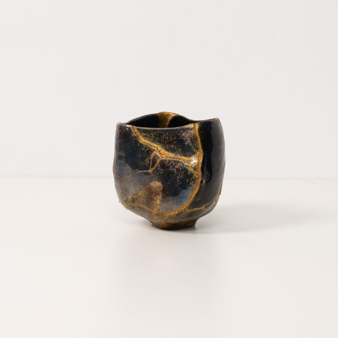 A black kintsugi matcha bowl stands on a white table displaying golden lightning lines of wabi sabi