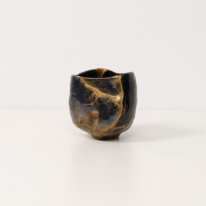 A black kintsugi matcha bowl stands on a white table displaying golden lightning lines of wabi sabi