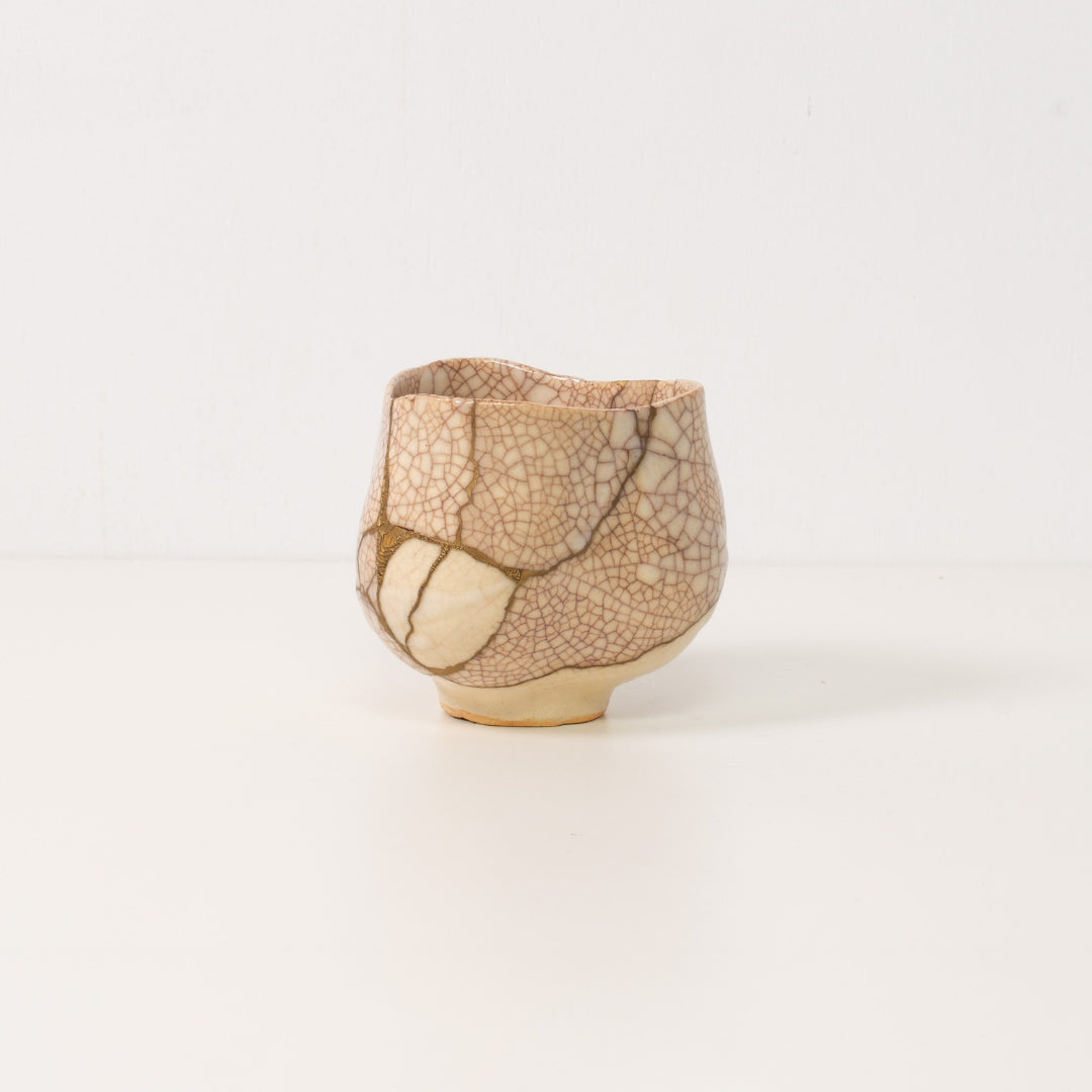 A white kintsugi matcha bowl rests beside a wooden box representing beautiful wabi sabi art and resilient pottery art