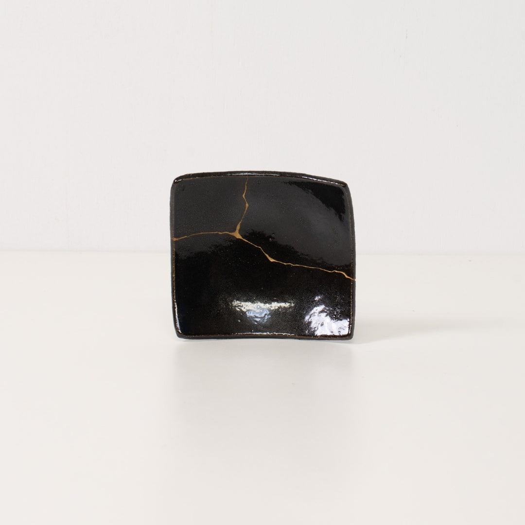 Close up of a black kintsugi plate revealing a bright golden lightning bolt repair symbolizing resilient pottery art