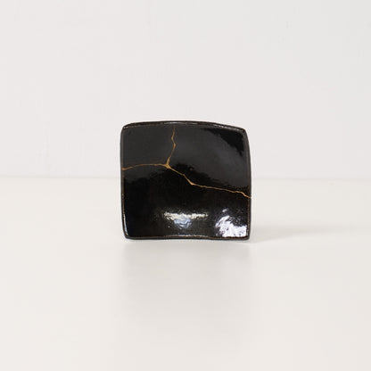 Close up of a black kintsugi plate revealing a bright golden lightning bolt repair symbolizing resilient pottery art