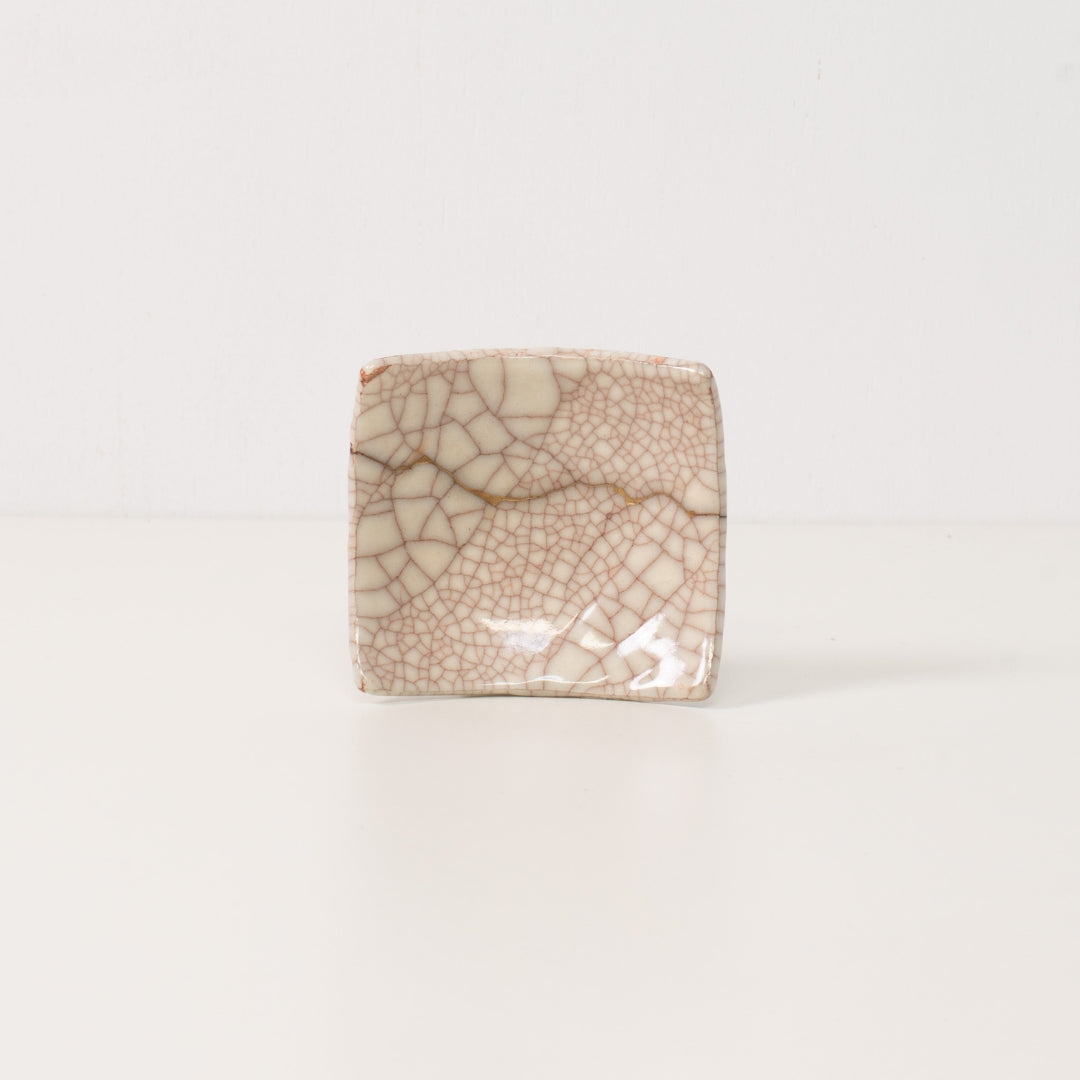 A square white kintsugi plate stands on a table displaying golden lines that represent wabi sabi resilience and beauty