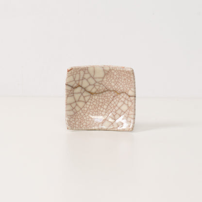 A square white kintsugi plate stands on a table displaying golden lines that represent wabi sabi resilience and beauty