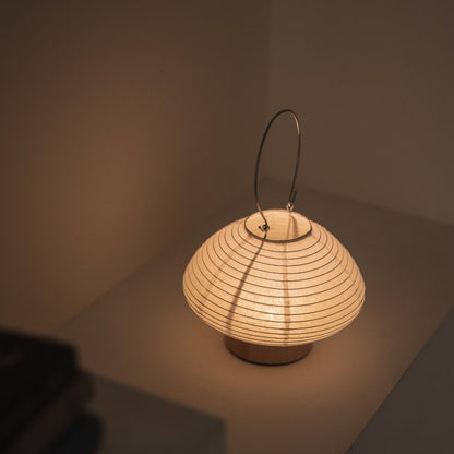 Overhead view of a lit portable lamp made of mino washi paper highlighting the ribbed structure and warm light