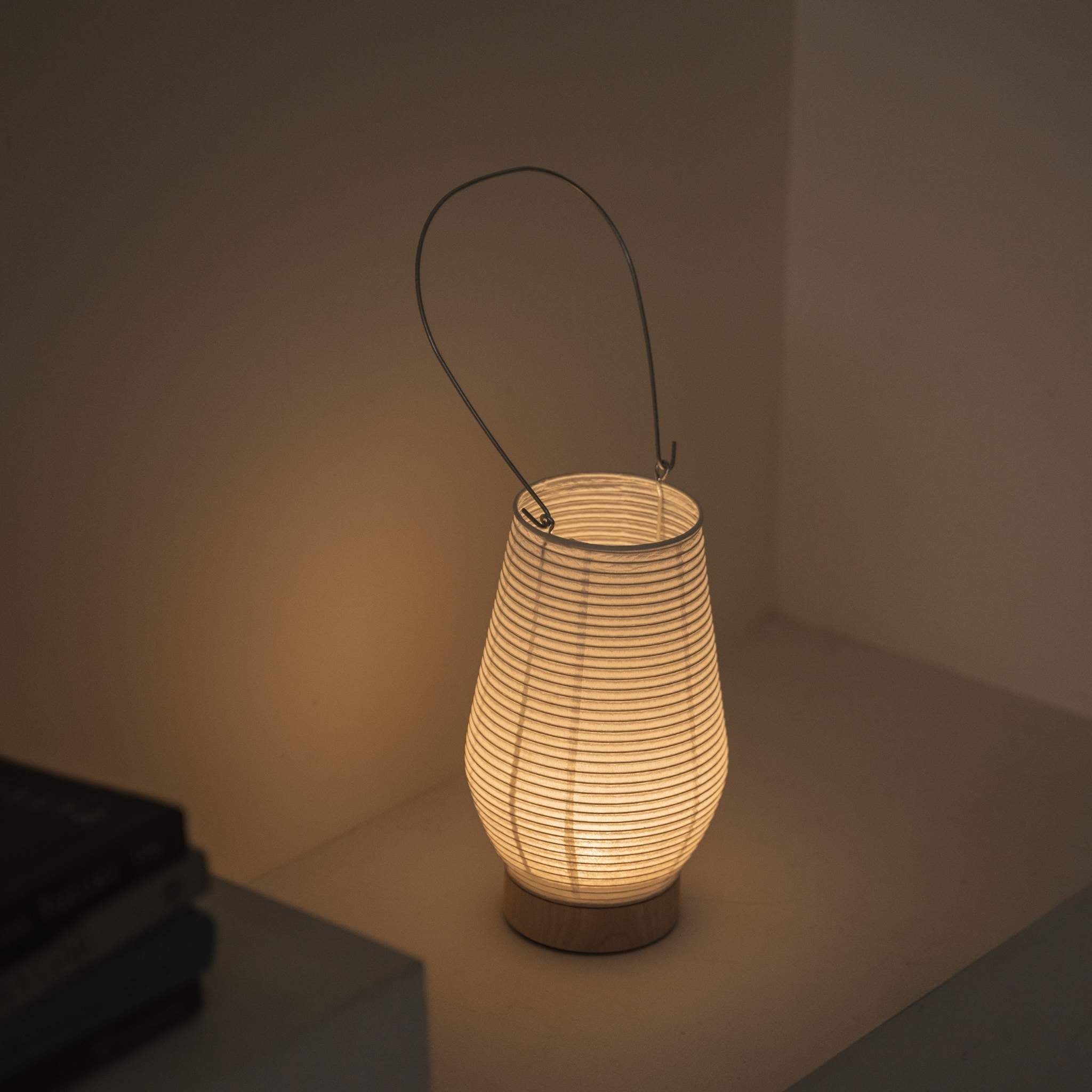 Overhead view of a lit portable lamp made of mino washi paper highlighting the ribbed structure and warm light