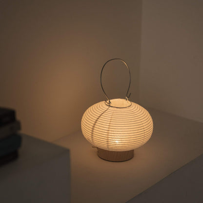 Overhead view of a lit portable lamp made of mino washi paper highlighting the ribbed structure and warm light