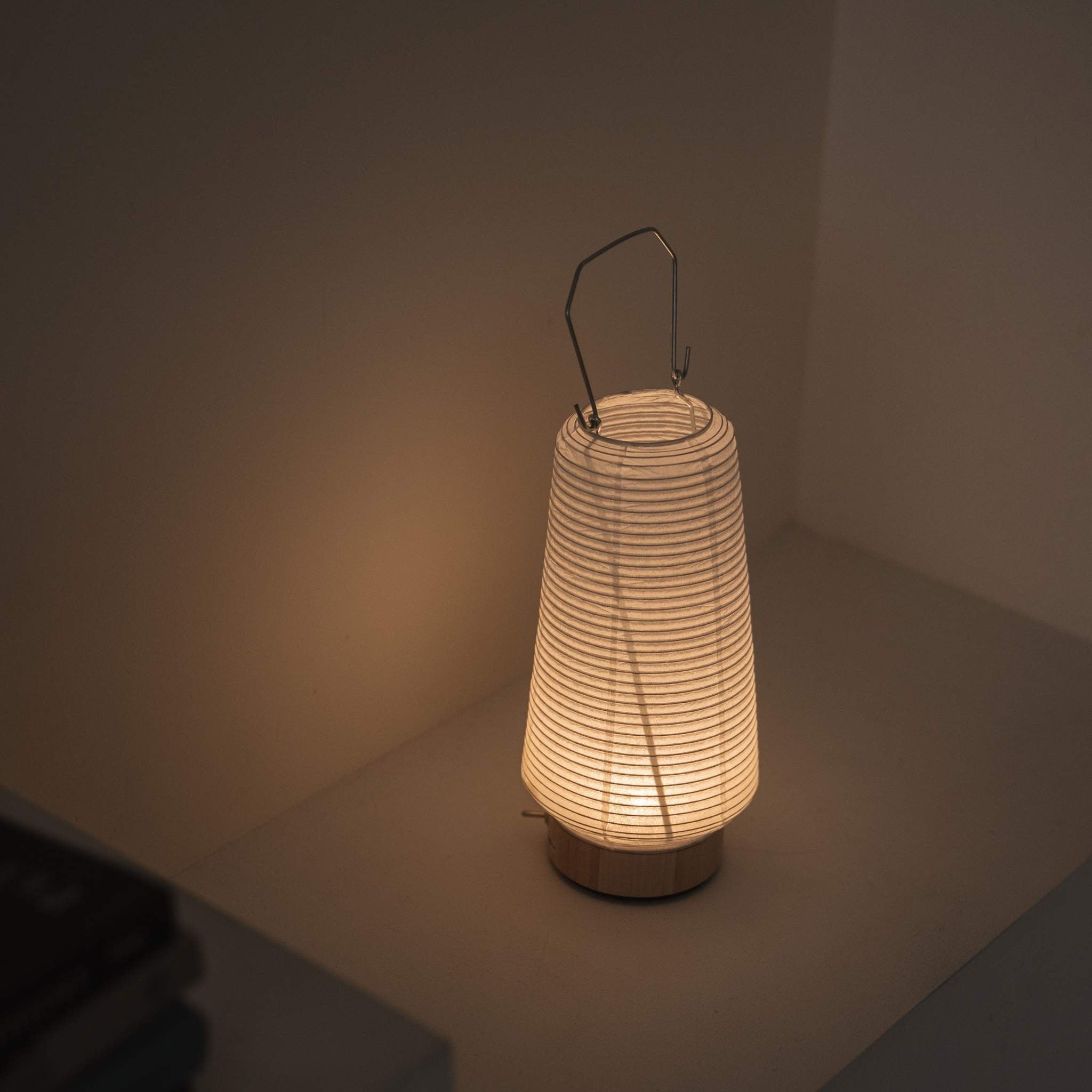 Overhead view of a lit portable lamp made of mino washi paper highlighting the ribbed structure and warm light