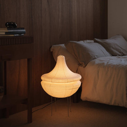 Illuminated Japanese paper floor lamp Gemini 02 glowing with warm soft light situated on the floor beside a bed in a Japanese bedroom