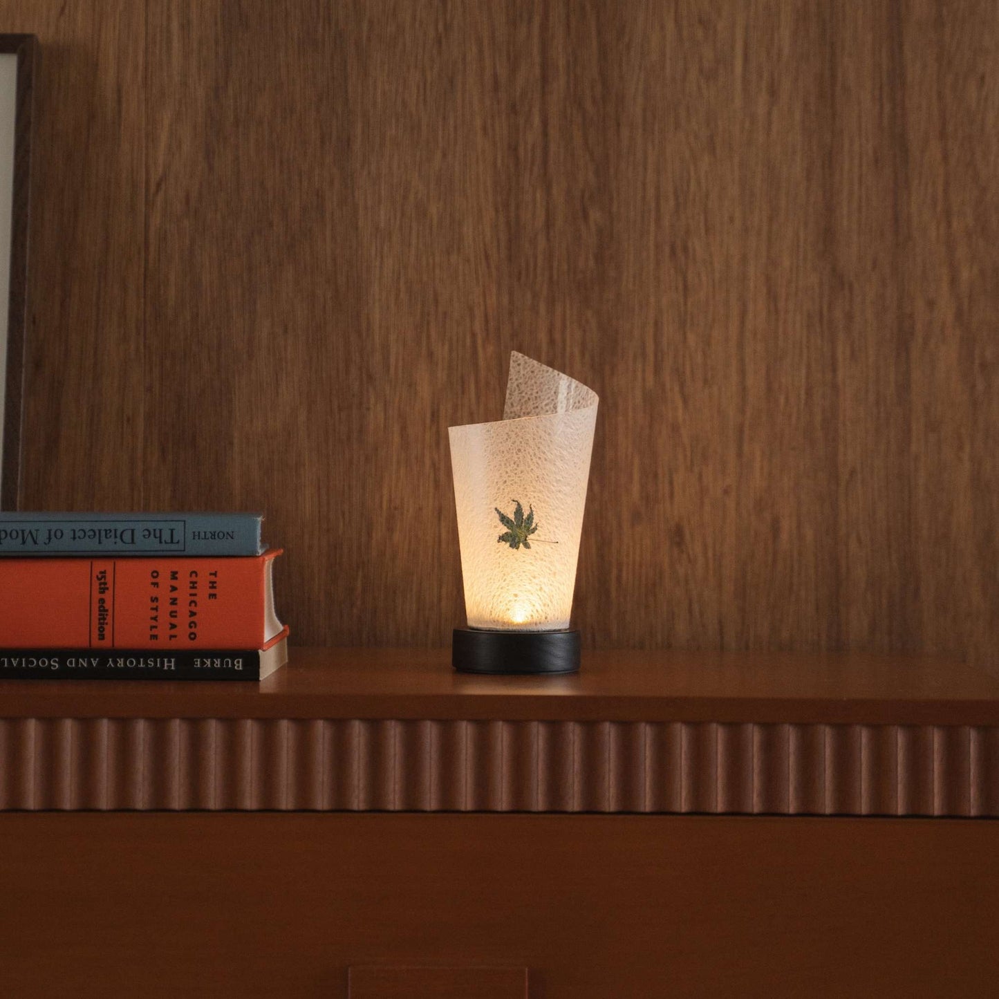 Lit Japanese paper table lamp "Maki" Momiji Leaf casting soft upward light as an ambient lamp on a mid-century modern console table.