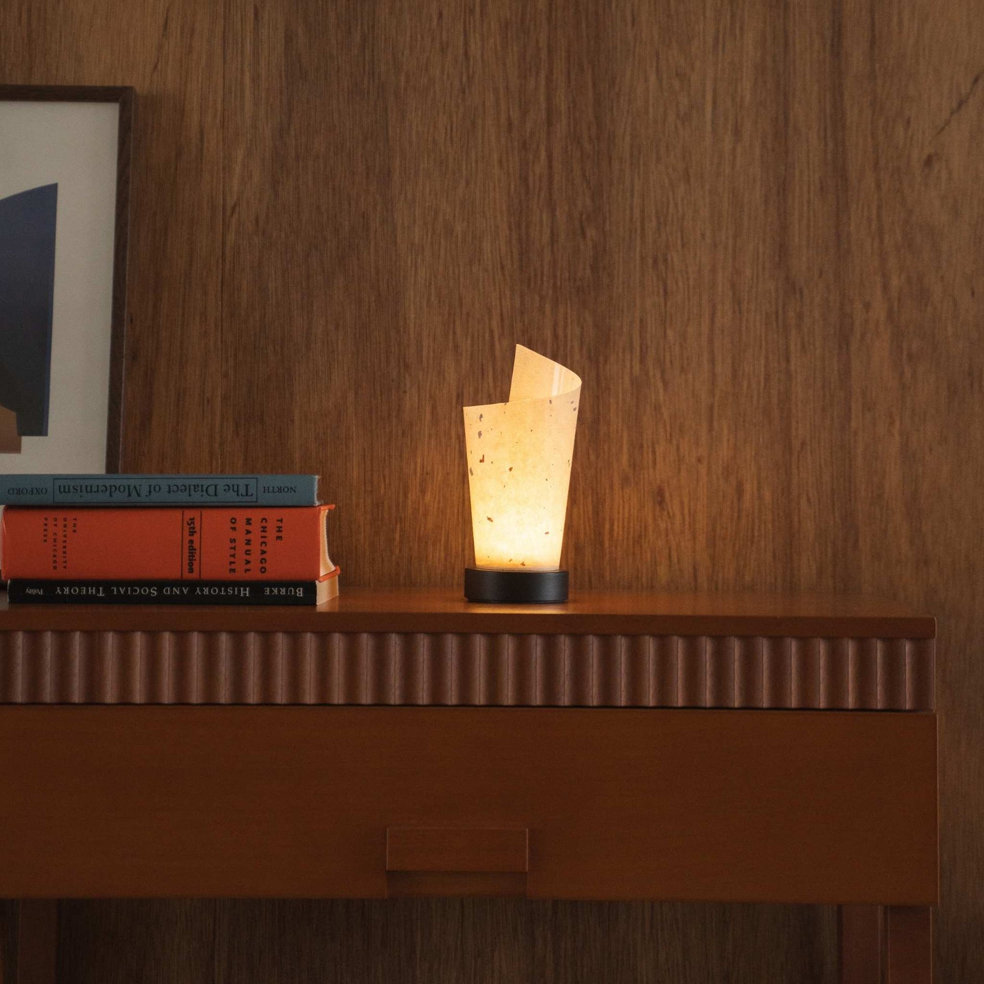 Lit Japanese paper table lamp "Maki" casting soft upward light as an ambient lamp on a mid-century modern console table.