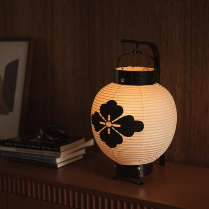 Glowing Japanese paper lantern featuring a black flower diamond crest design painted on warm white washi paper.