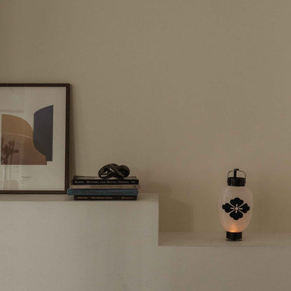 Japanese paper lantern with black flower motif displayed as an art object on a white Japandi living room shelf.