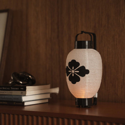 Close up of a glowing paper lantern chochin with a bold black hanabishi design on a wooden console table.