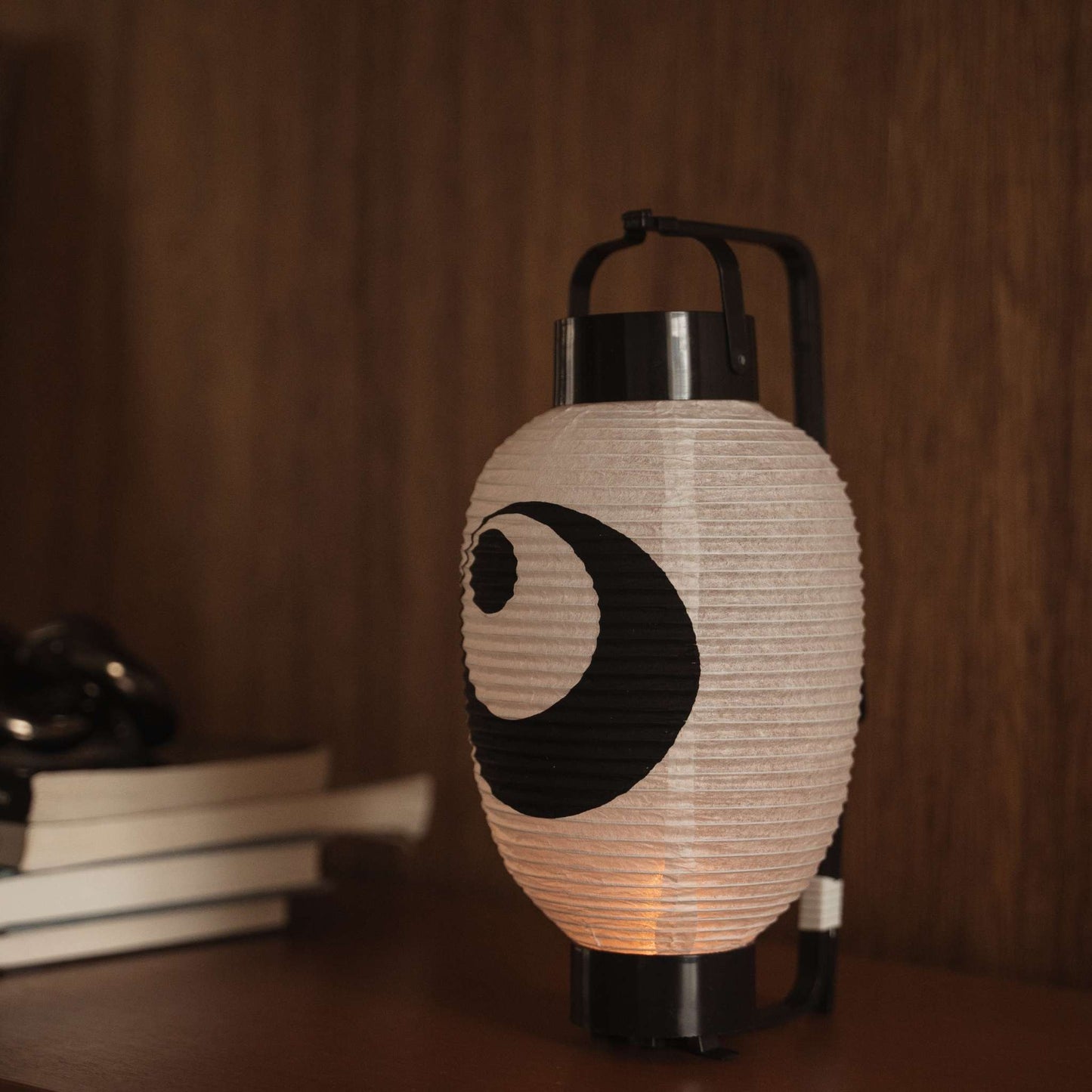 Lit Japanese paper lantern chochin on a dark wooden table displaying the traditional black ink design.