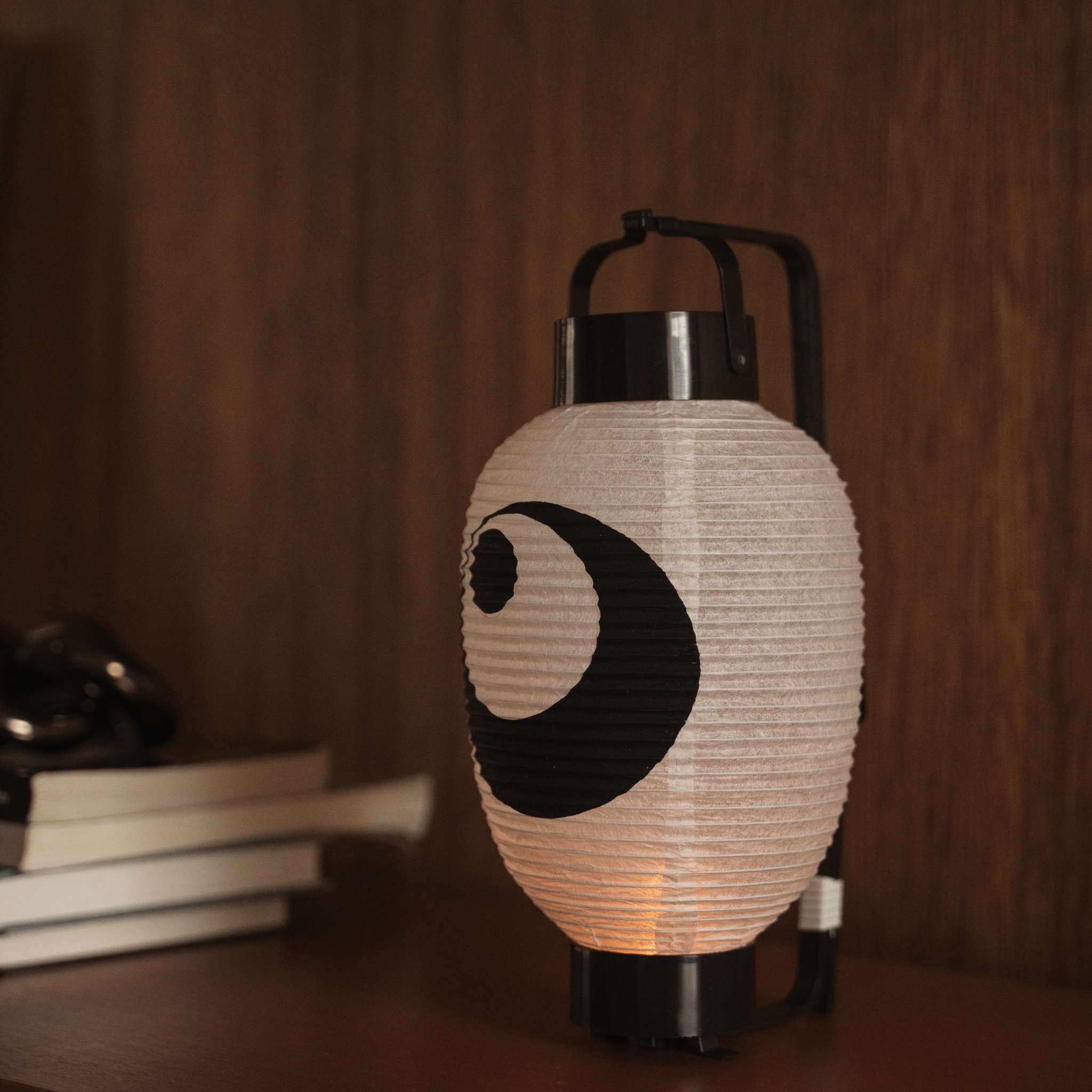 Lit Japanese paper lantern chochin on a dark wooden table displaying the traditional black ink design.