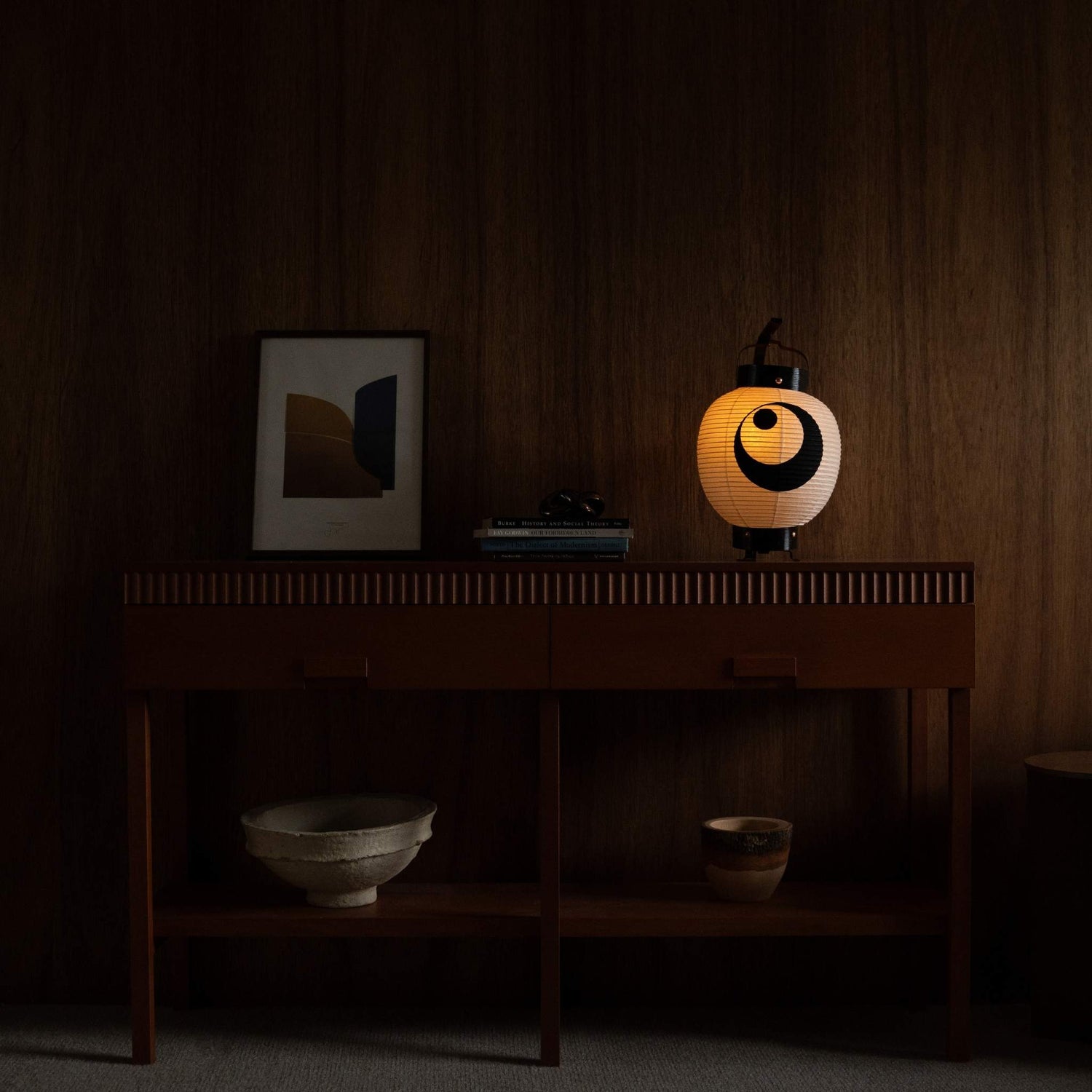 Lit Japanese paper lantern standing on a mid century modern console table adding warm ambiance to a living room.