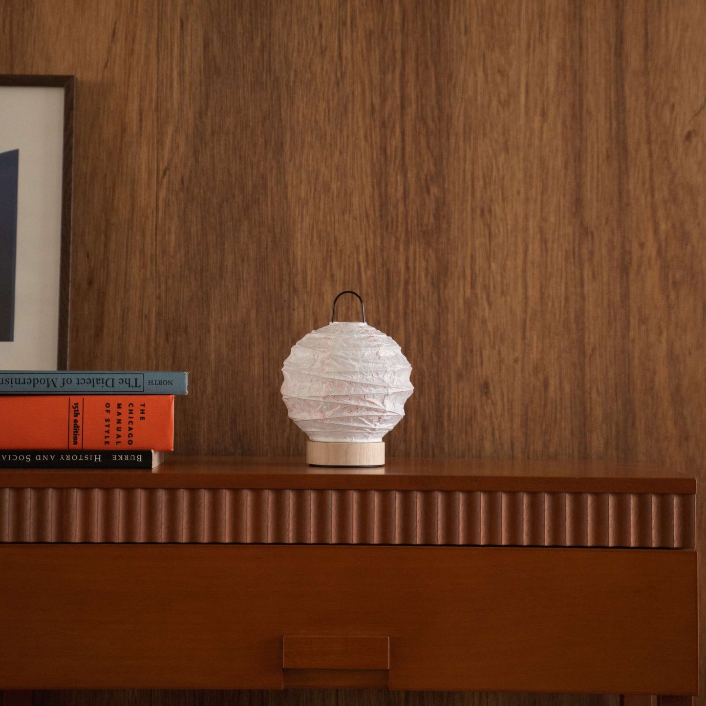 Unlit Japanese paper lamp with sakura patterns styled on a mid-century modern wooden console table.