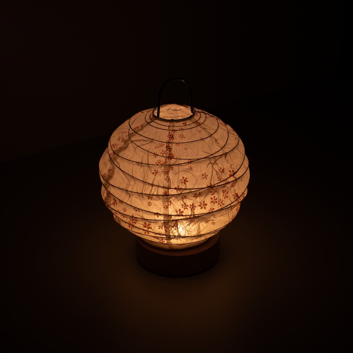 Japanese Paper Table Lamp "Yuhi" Sakura, white, Mino Washi paper - high angle view of lit Japandi style lamp with wire handle.