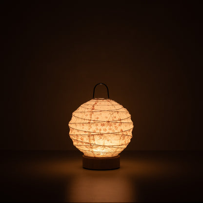 Japanese Paper Table Lamp "Yuhi" Sakura, white, Mino Washi paper - lit round paper lamp casting a warm glow in a dark room.