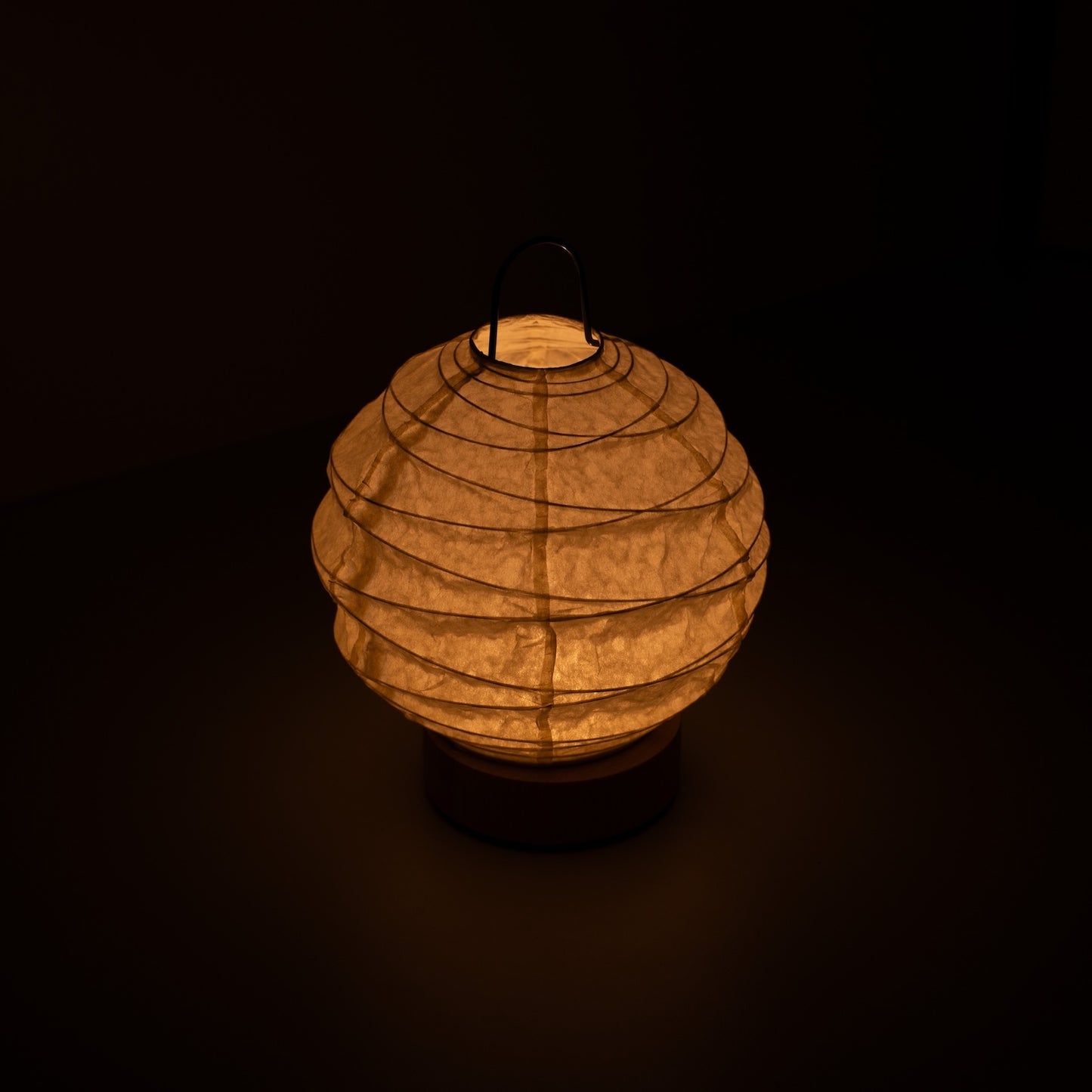 Japanese Paper Table Lamp "Yuhi", white, Mino Washi paper - high angle view of lit Japandi style lamp with wire handle.