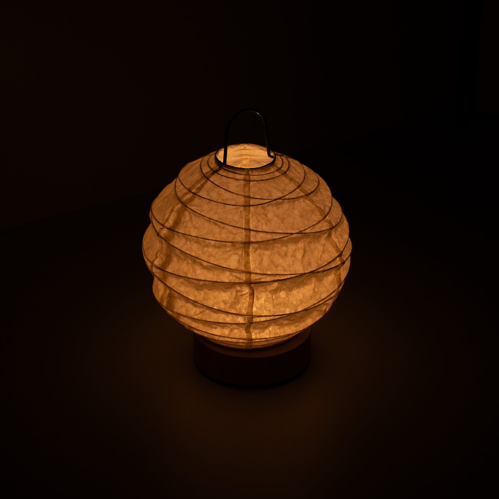 Japanese Paper Table Lamp "Yuhi", white, Mino Washi paper - high angle view of lit Japandi style lamp with wire handle.