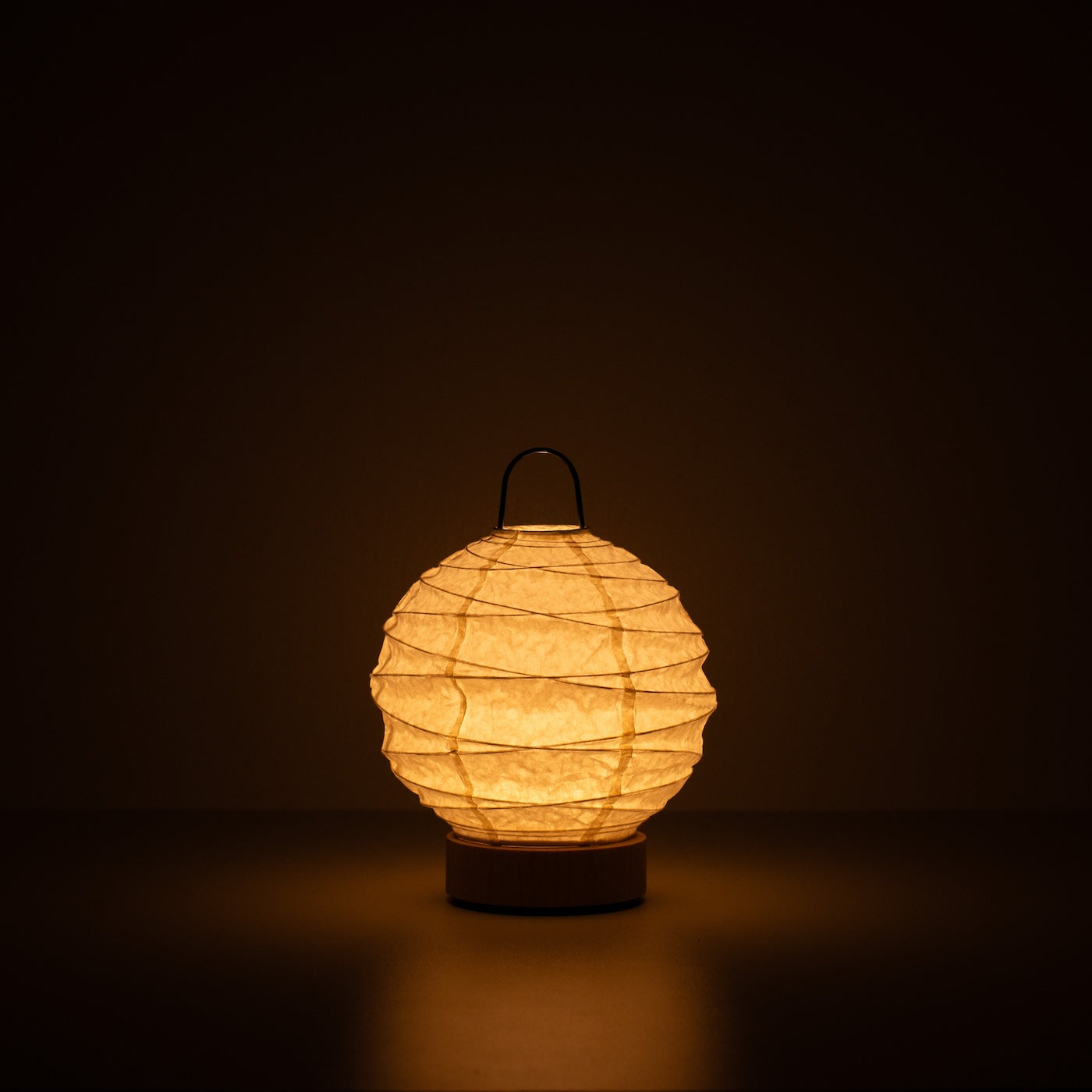 Japanese Paper Table Lamp "Yuhi", white, Mino Washi paper - lit round paper lamp casting a warm glow in a dark room.
